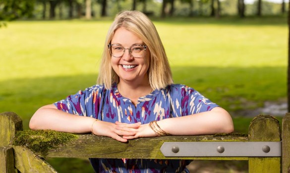 Headshot of a woman smiling to the camera leaning on a wooden gate.